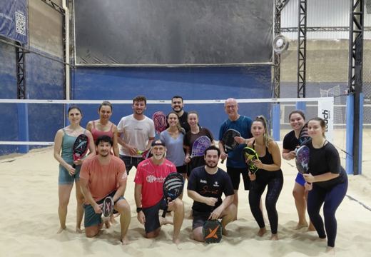 Turma de beach tennis no ambiente coberto, com rede, piso de areia e espaço para jogos em grupo.