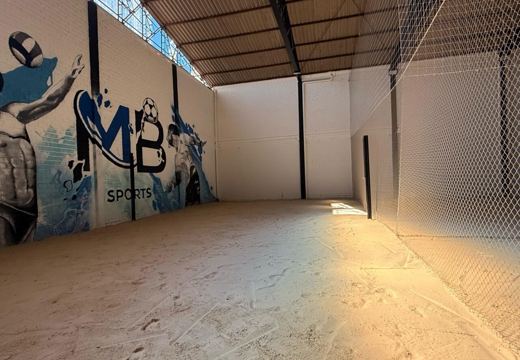 Quadra de areia coberta da MB Sports, com rede e mural da arena ao fundo.