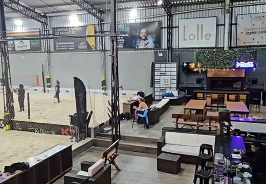 Vista interna da Play 820, com quadra de areia e área de convivência com bar, mesas e assentos.