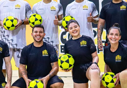 Grupo da escola de futevôlei do Rio Complex, na areia, com bolas e uniformes da arena.
