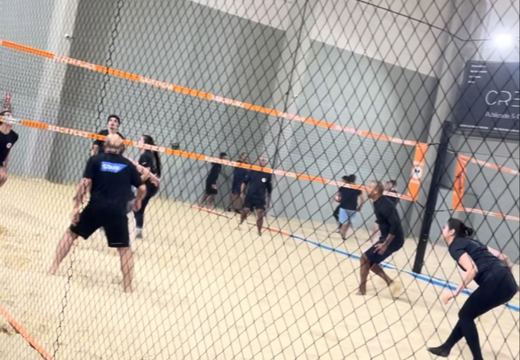 Partida de vôlei de areia em quadra coberta, com redes de proteção no complexo Beach Place.
