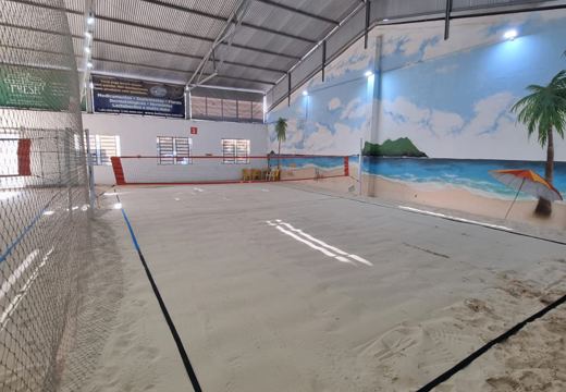 Quadra coberta da Beach Way Sports, com rede e mural de praia na lateral.