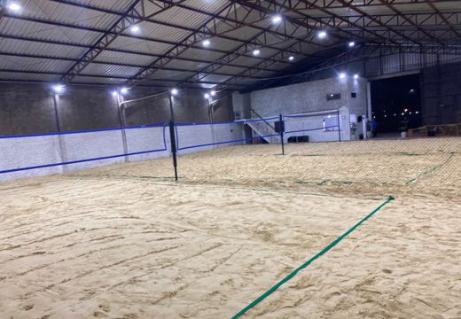 Vista das quadras de areia cobertas, iluminadas e separadas por redes de proteção.