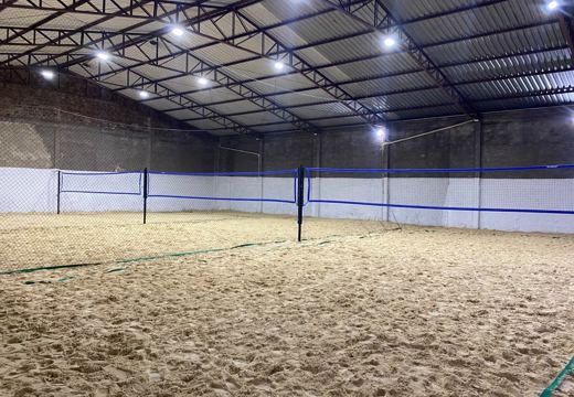Quadras poliesportivas cobertas da MTJ, com redes azuis e marcação na areia.